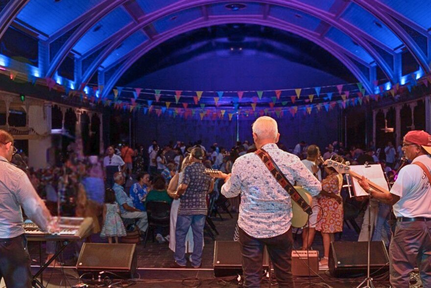 Looking at the back of a band on stage through to a theatre with the house lights on and people dancing.