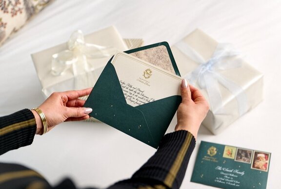Hands opening up Christmas themed Santa letters against a white background.