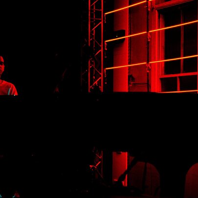 Pianist Josh Cohen playing a grand piano in a dark space lit only by red light. 