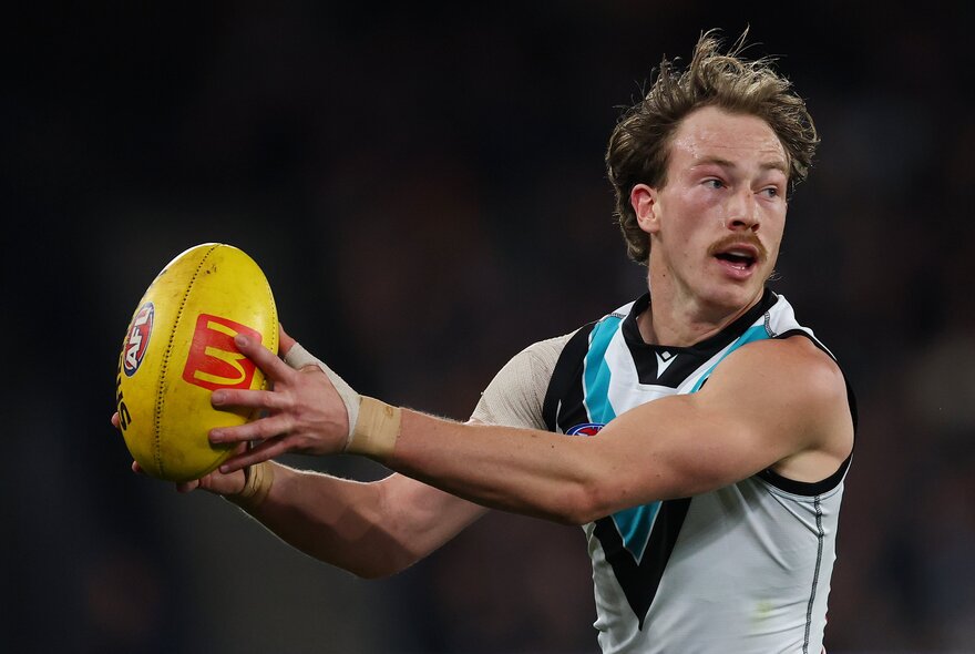 A Port Adelaide AFL player running and holding a yellow football.