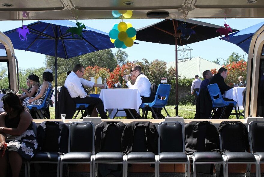 View from inside the boat outside to the banks of a river where people are seated at tables, eating and drinking.