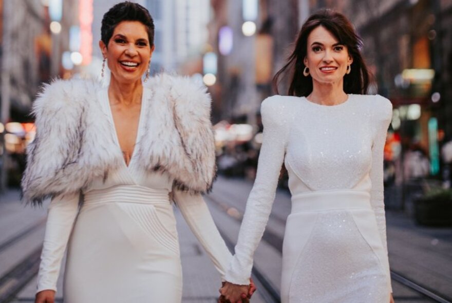 Two women holding hands, wearing white gowns.