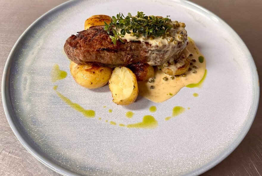 A steak dish with potatoes, creamy sauce and a green garnish.