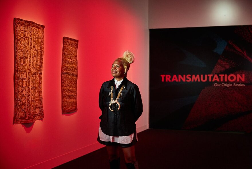 Papua New Guinea born multidisciplinary artist Weniki Hensch standing in a gallery space with red lighting and fabrics hanging on the wall. 