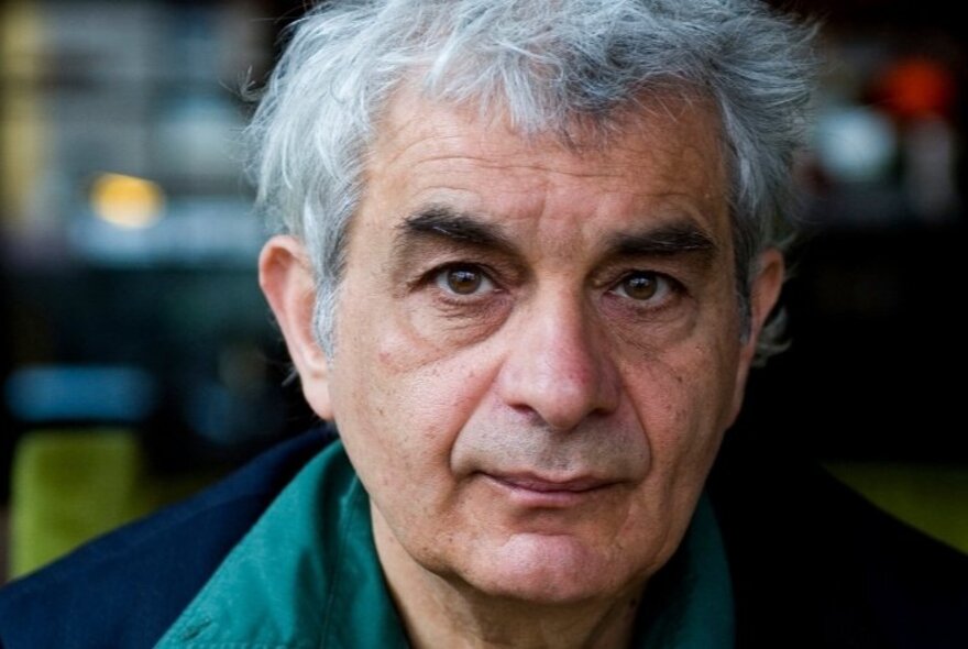 Close up of the face of poet PiO, a man in his 60s with white-grey hair and a neutral expression, looking directly at the viewer.