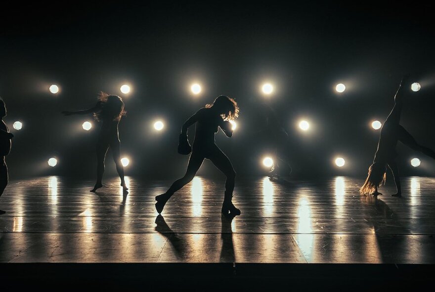 Three dancers on stage, silhouetted against the stage lighting.