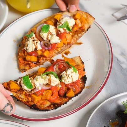 Hands dividing pizza into two slices on a plate.