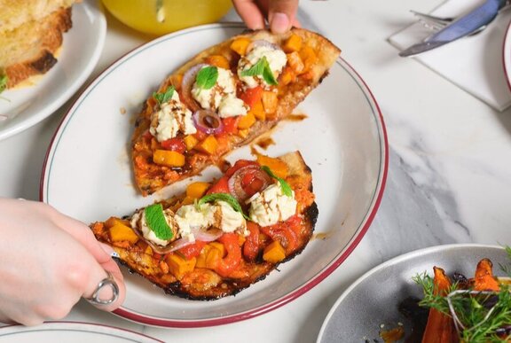 Hands dividing pizza into two slices on a plate.