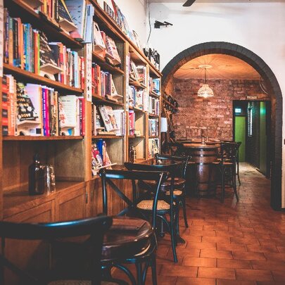 Cafe interior with bookcases lining the wall, wicker chairs and tables and view towards the back of the space.