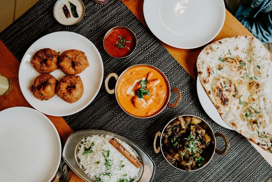 Bird's-eye view of various Indian dishes on a black table runner with white plates.