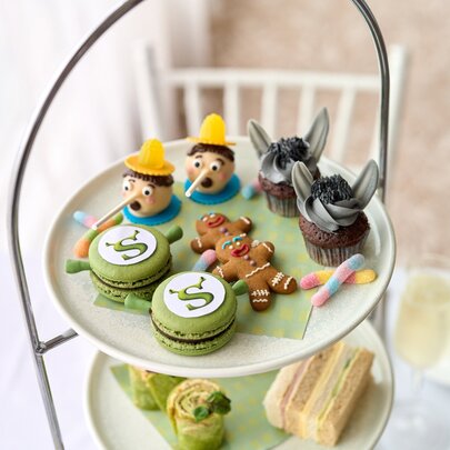 A multi-tiered high tea service featuring finger sandwiches, pastries, and sweets inspired by characters from the movie Shrek.