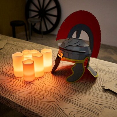 A wooden table displaying a Roman gladiator helmet constructed from cardboard and flat cardboard helmets awaiting construction, as part of a craft activity for kids at Melbourne Museum.