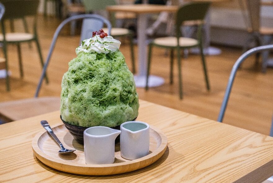 A large green shaved iced dessert with cream and red beans on top.