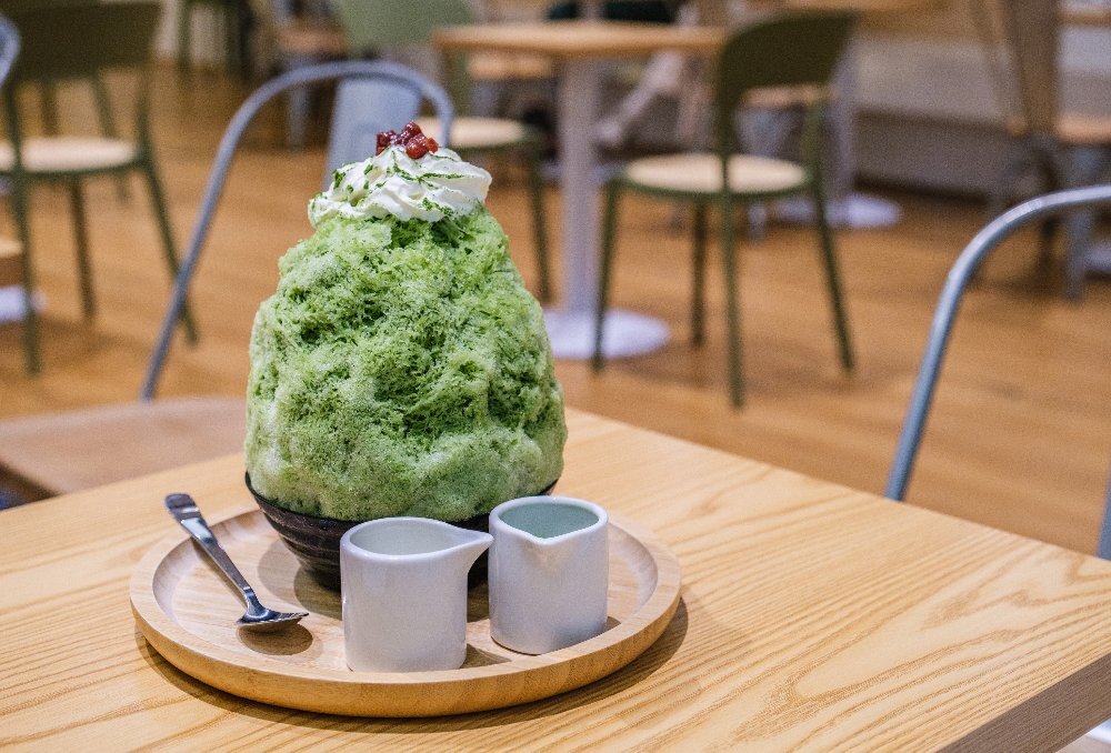 A large green shaved iced dessert with cream and red beans on top.