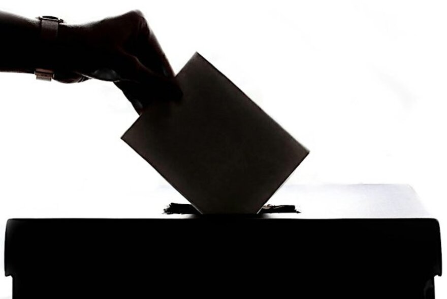 Hand putting a paper vote into a ballot box.