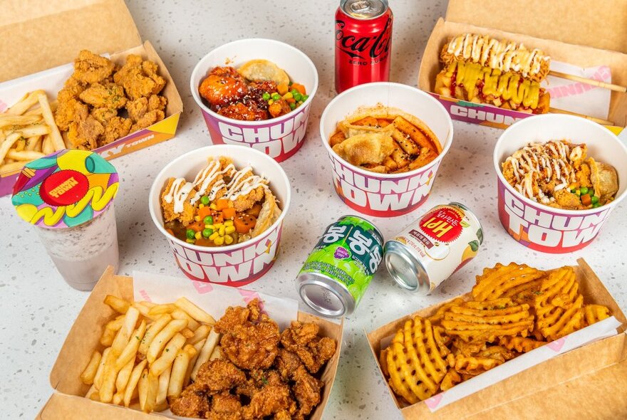 A table of takeaway food containers filled with food from Chunky Town including fried chicken, chips, hot dogs on sticks, cans of drink, and rice bowls.