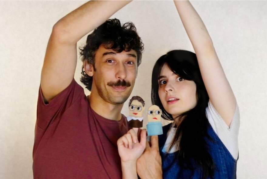 Two individuals with one arm raised above them, and with their other arm and hand holding finger puppets.