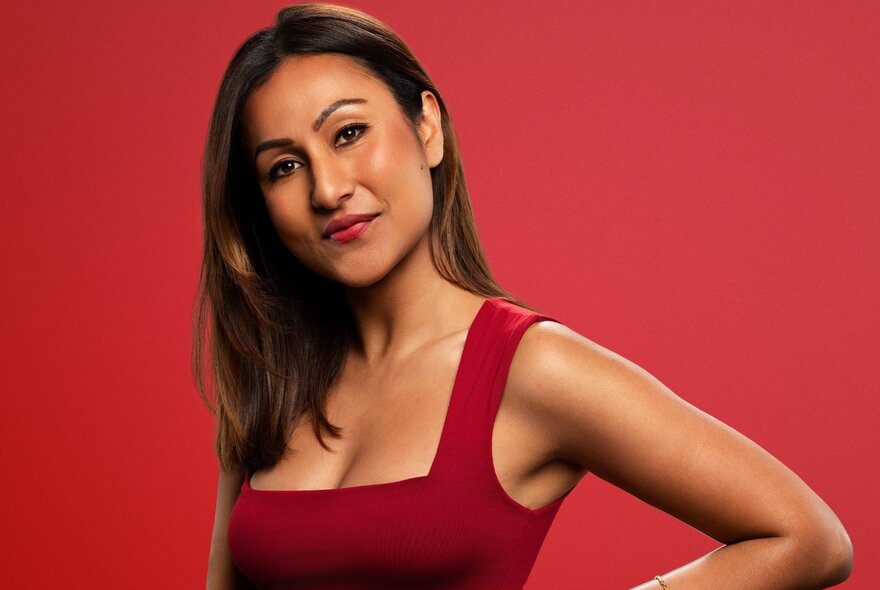 A woman in a red dress, with long brown hair, posed against a red background.