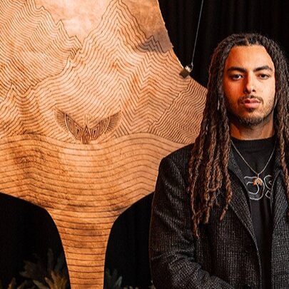 Man with dreadlocks standing in front of a kangaroo-skin artwork.