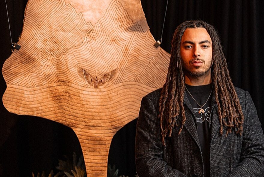 Man with dreadlocks standing in front of a kangaroo-skin artwork.