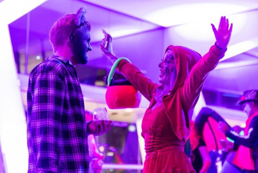 Two people greeting each other in Halloween costumes in front of a purple glassed area. 