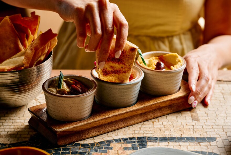 A hand dipping pita bread into a a trio of dips, on a restaurant table.