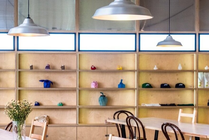 Relaxed cafe space with wall-shelf feature with ornaments, overhead industrial-style lighting, bentwood chairs and long tables.