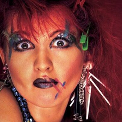 Singer dressed like Cyndi Lauper with bold makeup, alarmed expression and quirky jewellery.
