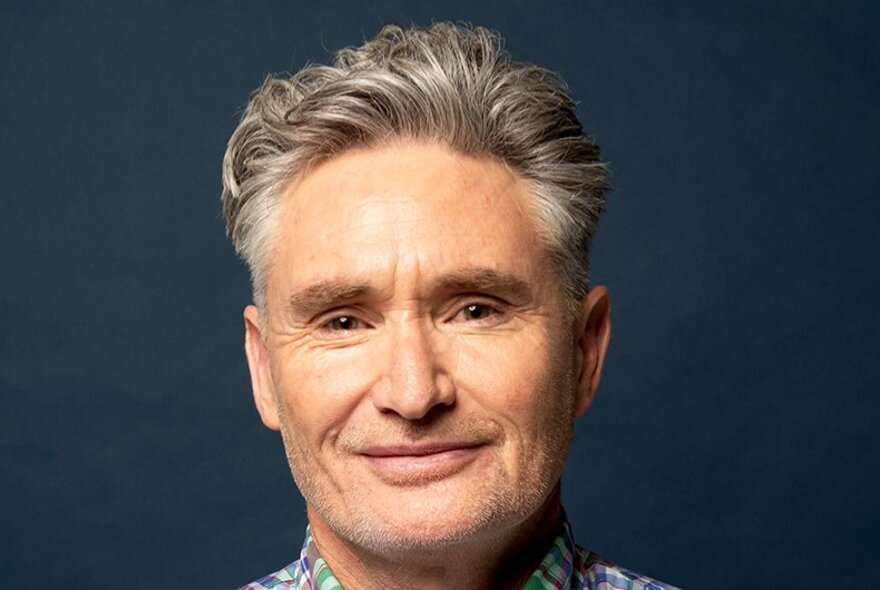 Headshot of comedian Dave Hughes, smiling softly and looking relaxed.