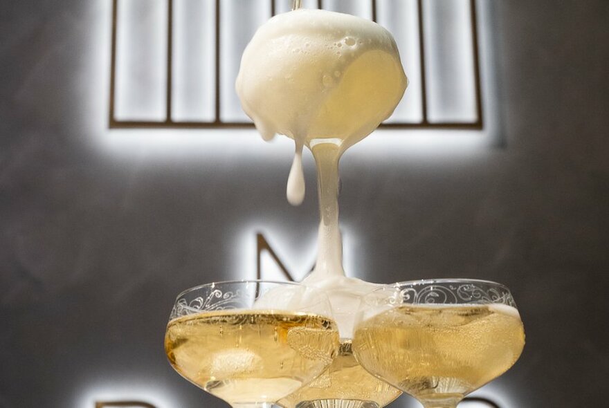 Sparkling wine bubbling over stacked champagne glasses.