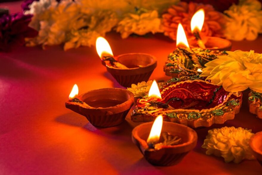 Clay lamps with flames on a red background with orange flowers.