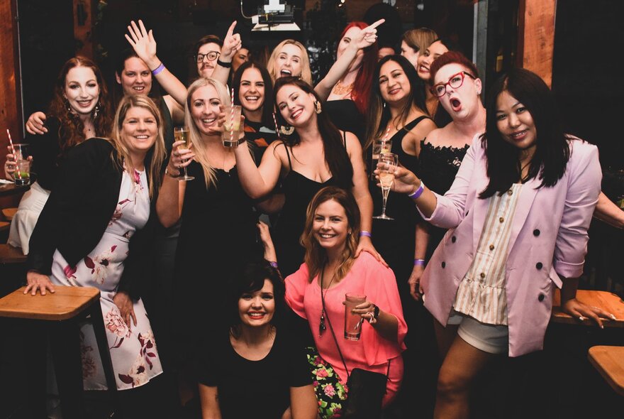 A large group of women partying and posing for a group shot with drinks in hand. 