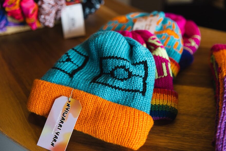 Hand knitted colourful beanies displayed on a table in a shop.