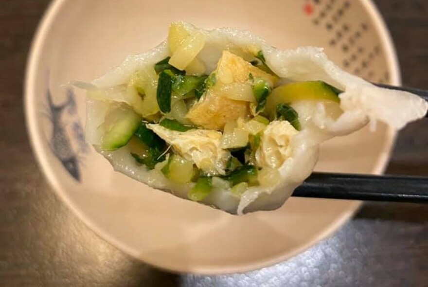 Chopsticks holding a steamed dumpling over a bowl.