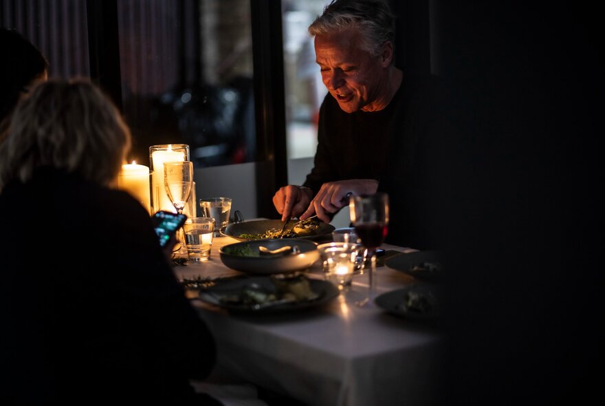 People seated across from each other at a dining table, with candles shining a soft light.