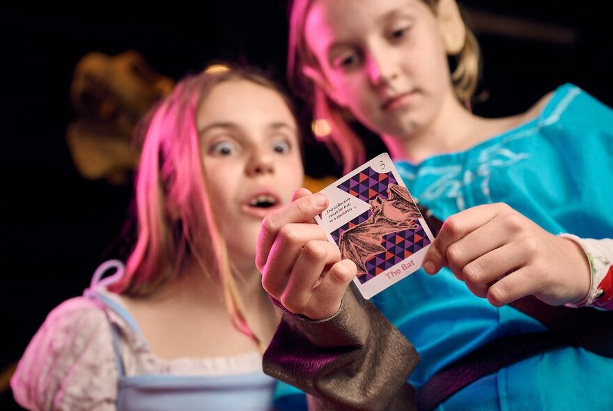 Two children dressed in Halloween costumes looking surprised as they read a card one of them holds in their hands.