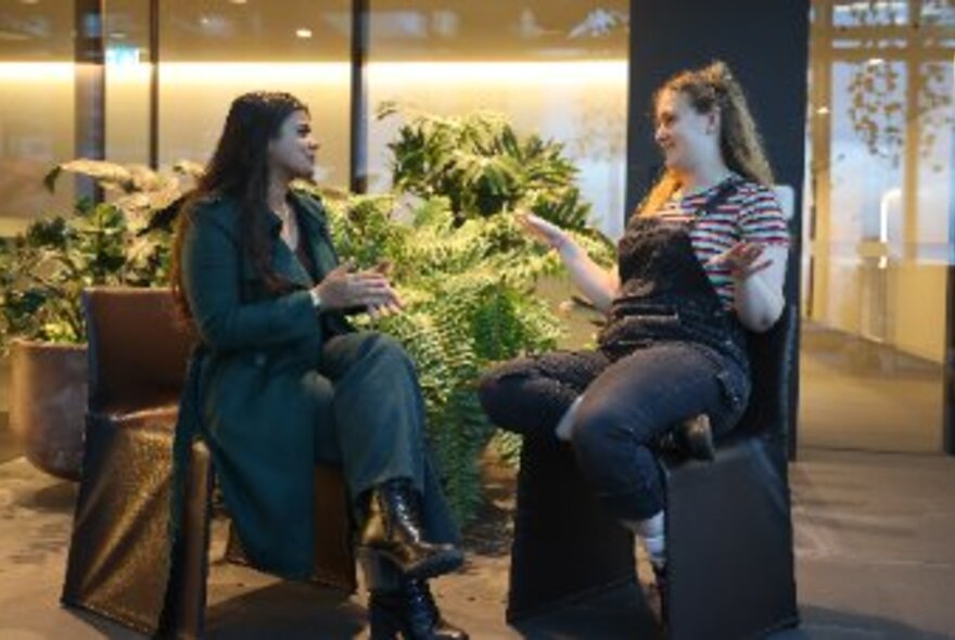 Two people seated opposite each other on chairs, talking to each other.