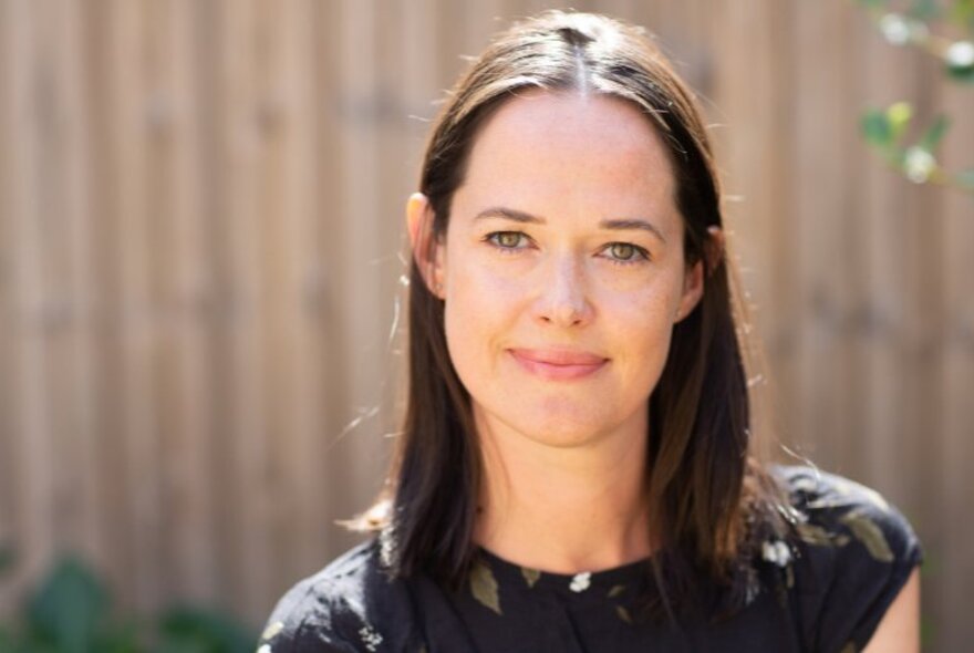 Author Sophie Gilbert with long dark hair and dark top, standing outside in the sunshine.