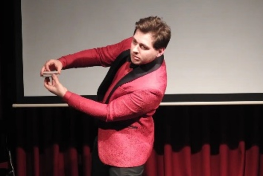 A magician in a pink jacket holding cards horizontally to his side. 