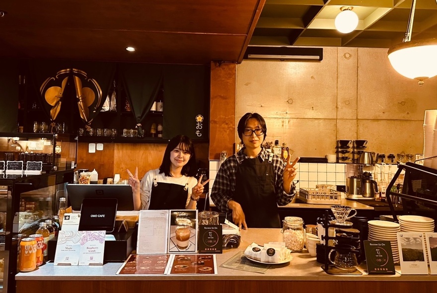 Two staff behind the service counter at Omo cafe, smiling and making a peace sign with their fingers.