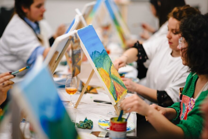 Workshop participants painting on small canvases, at a long workshop table.