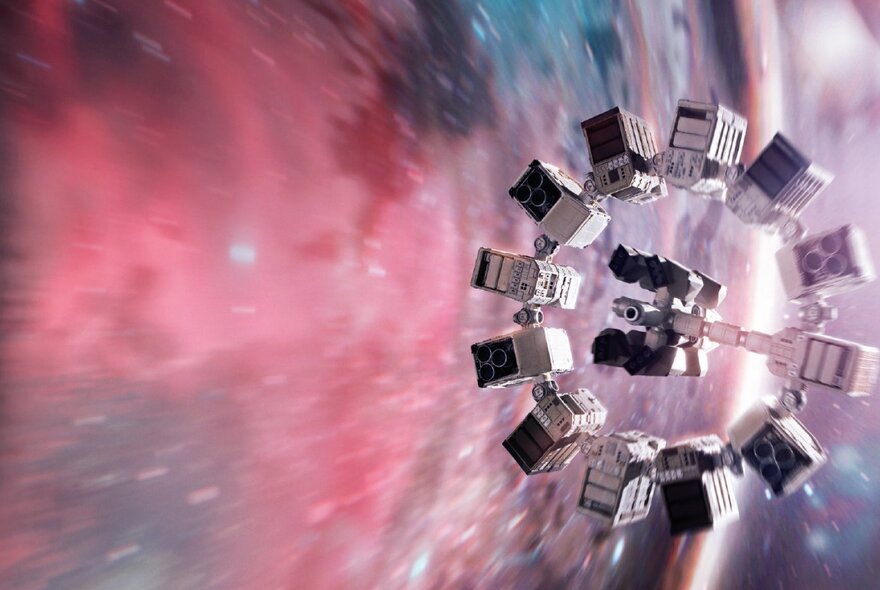 A still from the film, Interstellar, showing a circular space craft in front of a colourful wormhole in space.