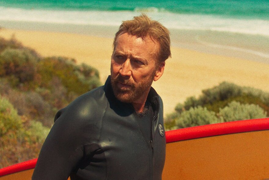 Nicholas Cage in a wetsuit at the beach in a still from the film The Surfer.