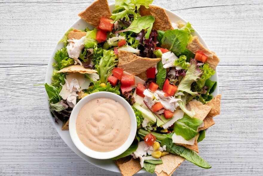 A colourful salad in a bowl with corn chips and a small bowl of dressing. 