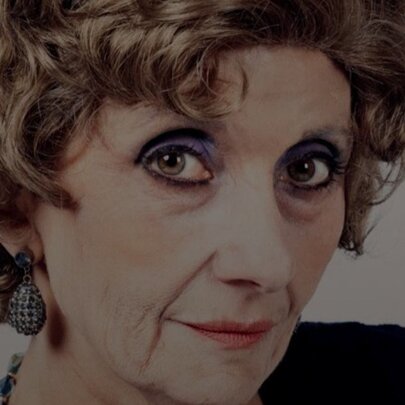 Close-up portrait of a woman with short, curly brown hair. She is wearing heavy, dark eye makeup.