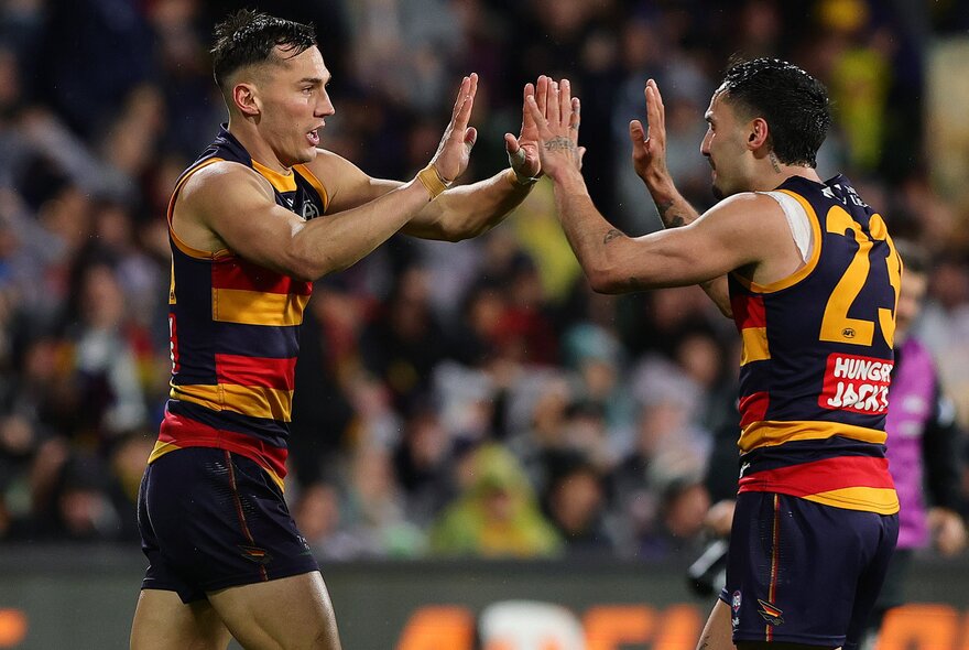 Two Adelaide Crows AFL players on the field about to high five each other.