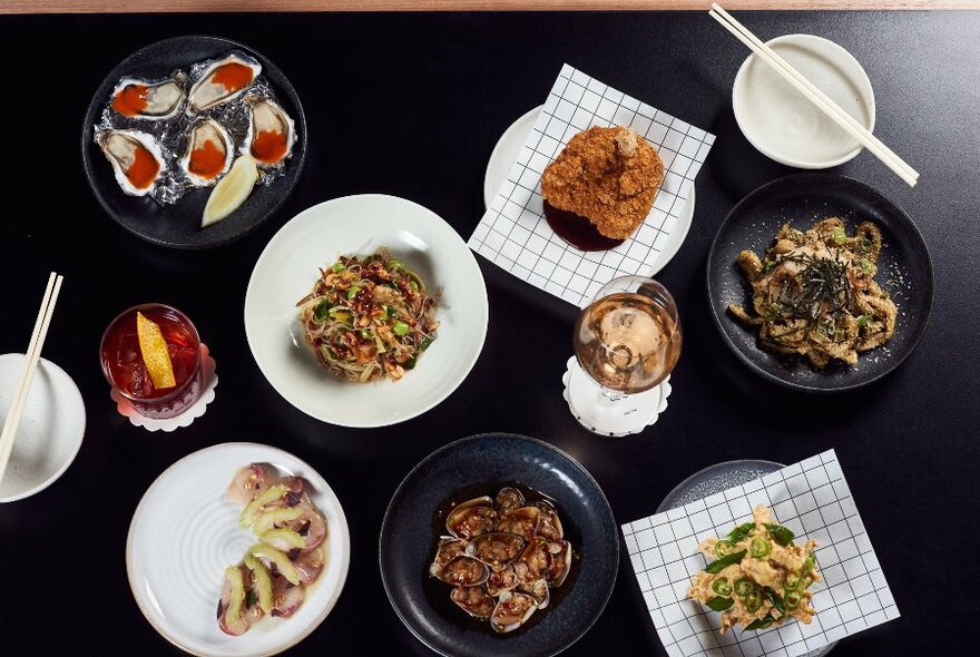 Overhead display of seven plates of food on a black table.