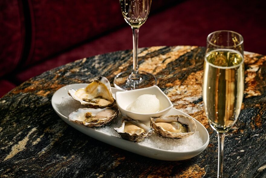 A table with an oval platter containing oysters and two champagne flutes. .