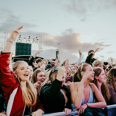A crowd of young music fans enjoying an outdoor concert from the front row railings. 