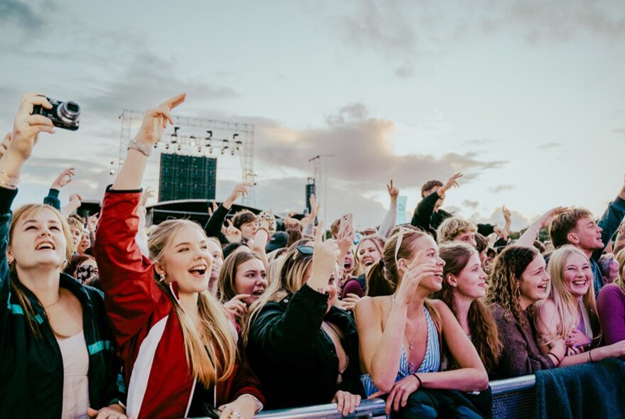 A crowd of young music fans enjoying an outdoor concert from the front row railings. 